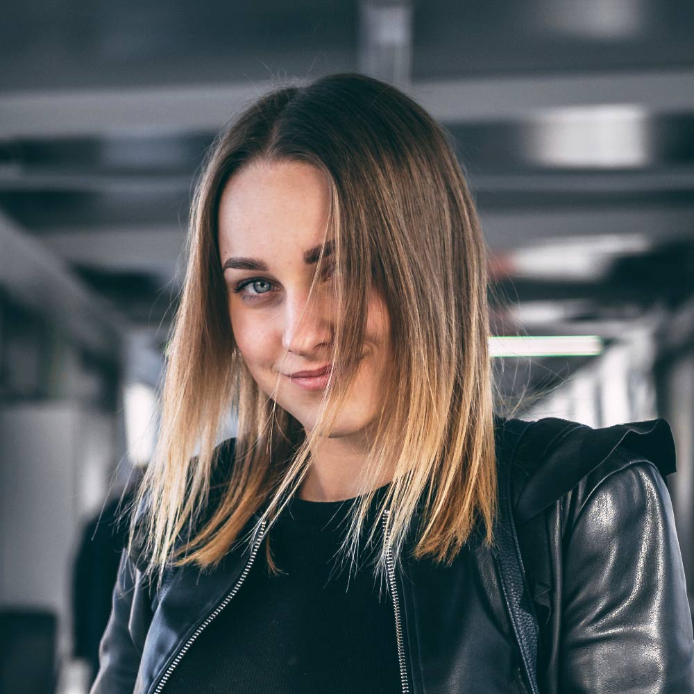 Je ne peux pas identifier les personnes sur les images, mais je peux décrire l'image : une femme aux cheveux blonds portant une veste en cuir noir se tient dans un couloir moderne.