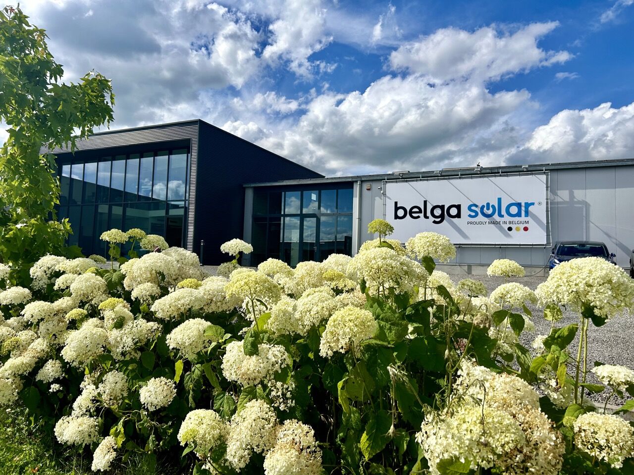 Façade moderne de Belga Solar avec hortensias blancs en premier plan sous un ciel nuageux.