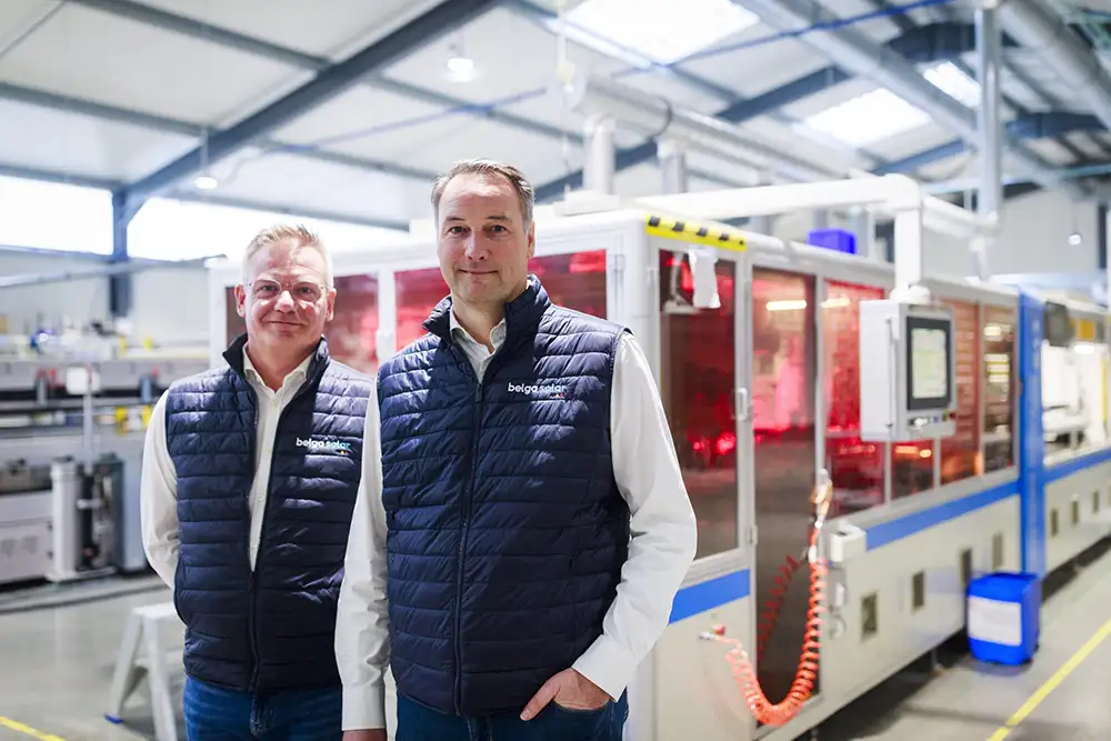 Deux hommes portant des gilets bleus se tiennent devant une machine industrielle dans un entrepôt lumineux.
