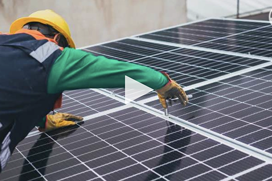 Un ouvrier en casque jaune installe des panneaux solaires noirs avec des gants, sur un toit.