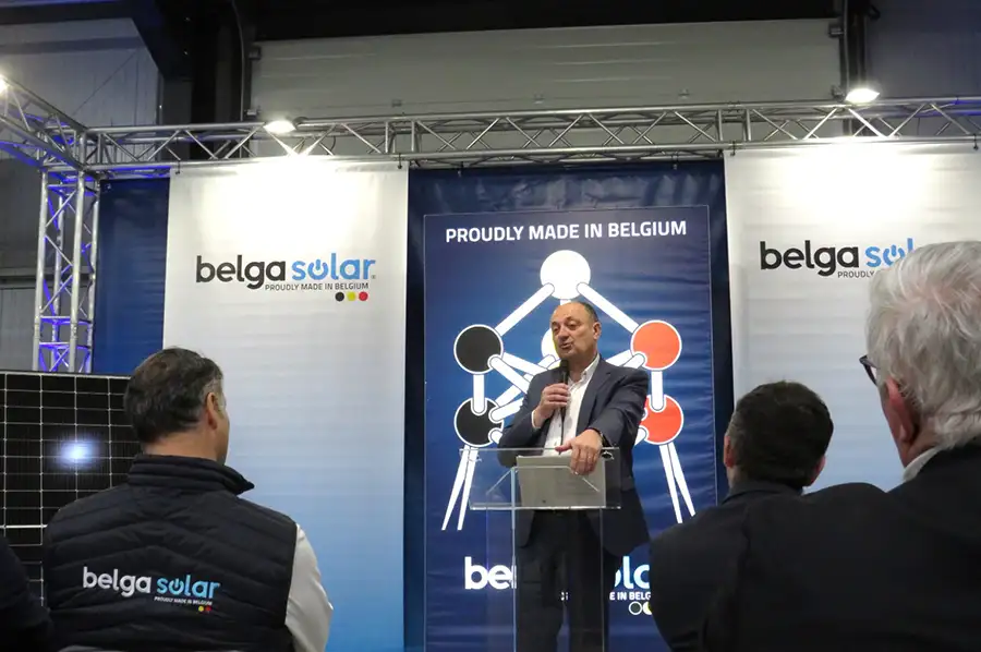 Un homme en costume parle à un podium devant un panneau "Proudly Made in Belgium" avec des logos Belga Solar.